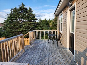 A wooden deck with a table and chairs, surrounded by a wooden railing, and a house with beige siding and a window.