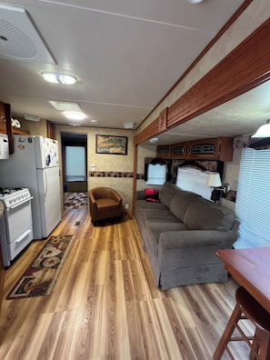 Indretning i en kompakt autocamper med et tekøkken, en sofa, et lille bord og en gulvtæppe med et mønster.