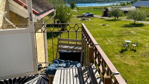 Un balcone con vista su un lago, una zona verdeggiante con tavolo e sedie, e un edificio con tetto spiovente.