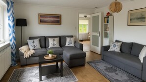 Un soggiorno moderno con un divano angolare grigio, un tavolino da caffè e un tappeto decorato. Si vede una libreria con libri e oggetti decorativi, e un quadro appeso alla parete.