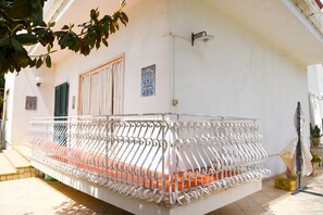 Een balkon met een witte metalen hekwerk, een deur en een wandlamp.
