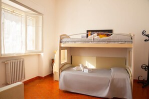 Ein Schlafraum mit Etagenbetten, einem Heizkörper, einem Fenster mit Vorhängen und einem kleinen Tisch.