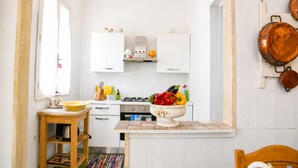 Una cocina con gabinetes blancos, una estufa a gas, una mesa de madera y un colgador para ollas.