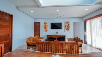 Uma área de refeições com mesa e cadeiras de madeira, ventilador de teto e obras de arte nas paredes.