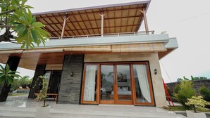 Una casa moderna de dos plantas con techo plano, grandes puertas correderas de vidrio y un balcón.