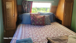 Une chambre d’habitation aménagée dans un Galaxy S20 FE 5G, avec un couvre-lit à motifs, des coussins et une fenêtre donnant sur un paysage verdoyant.