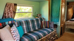 Un intérieur de camping-car accueillant, avec un canapé à rayures, une fenêtre avec des rideaux et une petite table agrémentée d’une plante.