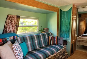 A cozy RV interior with a striped sofa, a window with curtains, and a small table with a plant.