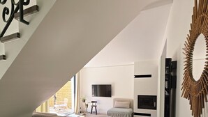 Un loft moderne doté d’un escalier, d’un espace de vie avec un canapé et un pouf, d’un téléviseur et d’un élément décoratif mural.
