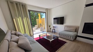 Un salon moderne comprenant un canapé, une petite causeuse, une table basse en verre et un téléviseur fixé au mur.
