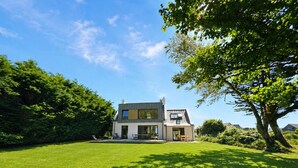 Une maison moderne à deux étages, dotée d’une grande pelouse et d’un arbre en premier plan.