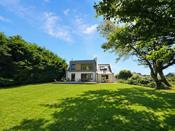A modern two-story house with a large lawn and a tree in the foreground.