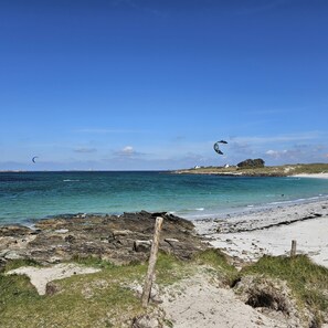 Een strand met heldere lucht, een rotsachtige kustlijn en een vergezicht op huizen.