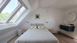 Ein Schlafzimmer mit einem großen Bett, einem Oberlicht, einem Nachttisch, einem wandmontierten Schminktisch und einem runden Spiegel.