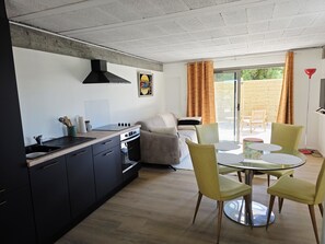 Una cocina moderna con estufa integrada, campana extractora negra y comedor con mesa de vidrio y sillas amarillas.