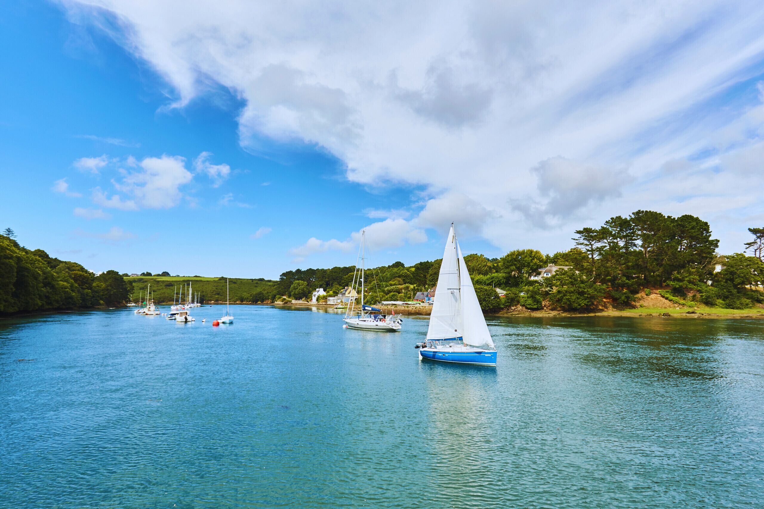 A calm river with sailboats and a house on the shore.