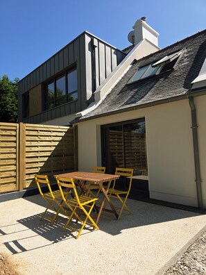 Una casa moderna con un patio, una mesa y sillas de madera, y un jardín cercado.