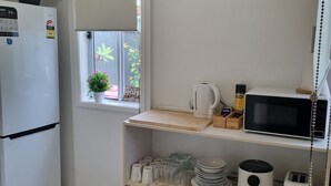 A kitchen with a white refrigerator, a microwave, a coffee maker, and a shelf with dishes and cookware.