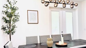 Een eetruimte met een donker houten tafel, grijs gestoffeerde stoelen, een geweven vaas en een kroonluchter met bolvormige lampen.