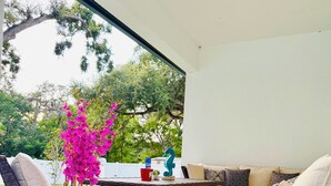Een terras met rieten meubilair, een bloempot en uitzicht op bomen.