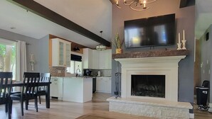A modern living room with a fireplace, a dining area, and a kitchen in the background.