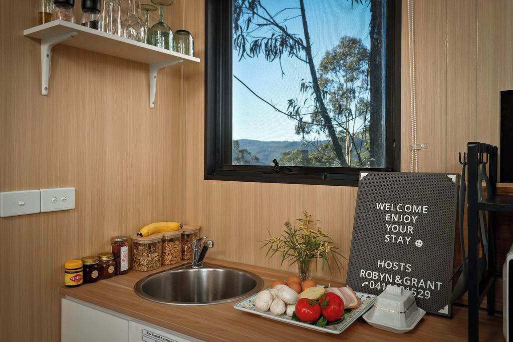 A kitchen with a stainless steel sink, wooden cabinets, a window with a view of trees, and a welcome sign.