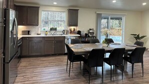 A modern kitchen with dark wood cabinets, a stainless steel refrigerator, and a dining area with a wooden table and black chairs. - Dacha in Hoodsport w/Hot tub (Hoodsport)