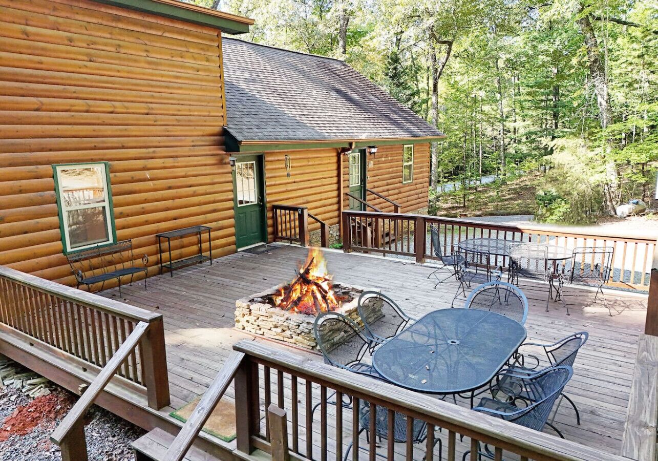 A wooden cabin with a deck, a fire pit, and outdoor furniture.