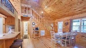 A wooden cabin interior with a dining area, kitchen, and a staircase leading to a loft. - S`more Waggin` Cabin: Pet-Friendly--wifi, firepit, pool table (Blue Ridge)