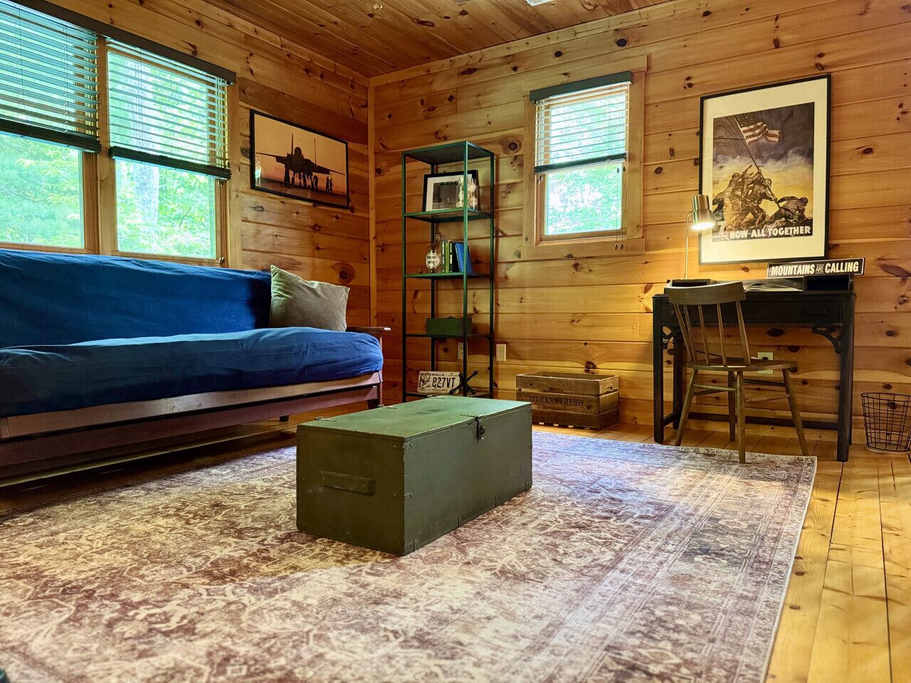 L’intérieur d’une cabane en rondins, avec un canapé bleu, une boîte de rangement verte, un tableau encadré et un bureau avec une chaise.