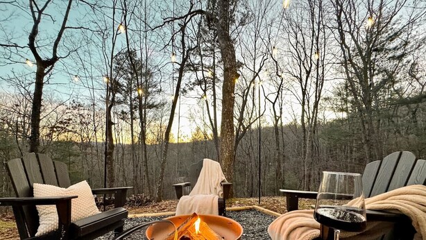 A cozy outdoor seating area with a fire pit, two Adirondack chairs, and a glass of wine. - The Tree House- Wifi- Firepit- 2 Fireplaces-Garden Tub-Free Activities (Morganton)