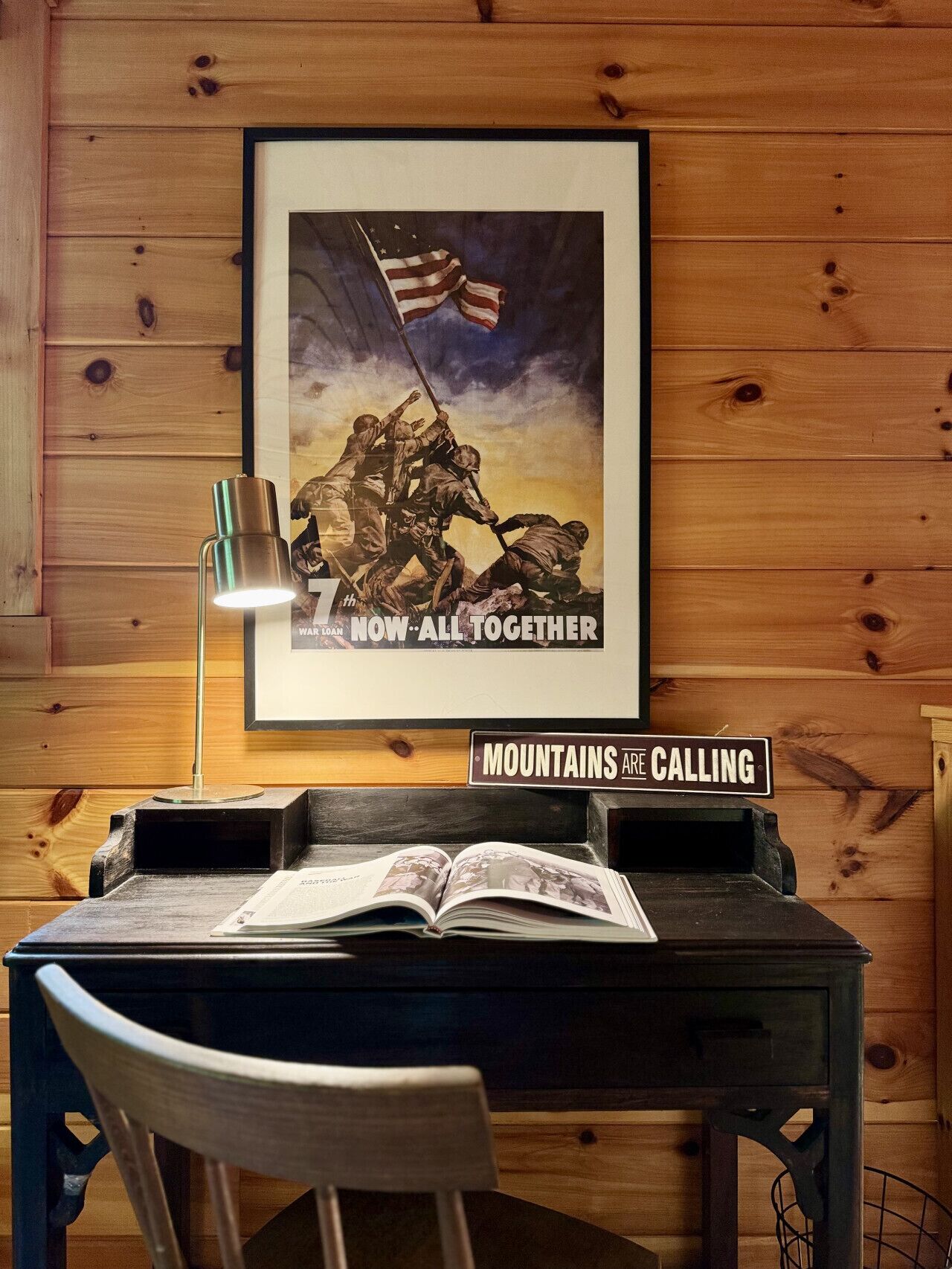 Un mur en bois orné d’une affiche encadrée représentant des soldats hissant le drapeau américain, un bureau avec une lampe et un livre ouvert.