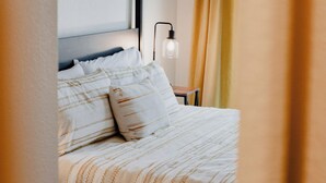 Un lit bien fait, avec une literie à rayures, une table de chevet avec une lampe et un rideau tiré en partie sur le côté.