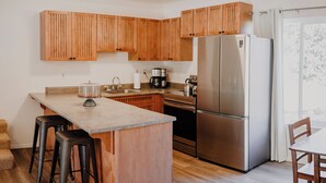 Une cuisine avec des meubles en bois, un réfrigérateur en acier inoxydable, une machine à café et un petit îlot central avec des tabourets.