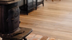 Une pièce avec un poêle ancien, une étagère en métal sur laquelle est posée une photo encadrée et une petite table en bois.