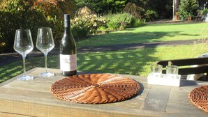 Un tavolo con due bicchieri da vino, una bottiglia e un sottopentola intrecciato.