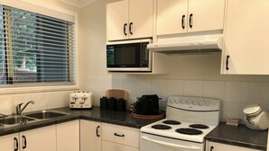 Una cucina con mobili bianchi, un fornello, un forno a microonde, un tostapane e un lavandino.