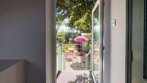 Blick durch eine Glastür auf eine Terrasse mit Gartenmöbeln und einem rosa Sonnenschirm.