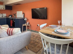 A compact living space with a kitchenette, a dining area with a table set for two, and a sofa.