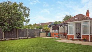 Ein Garten mit gepflegtem Rasen, Holzzaun und einem Haus mit Terrasse und überdachtem Bereich.
