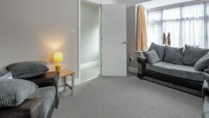 Ein Zimmer mit einer Couch, einem kleinen Tisch mit einer Lampe, einem gemusterten Teppich und einer Tür zu einem anderen Raum.