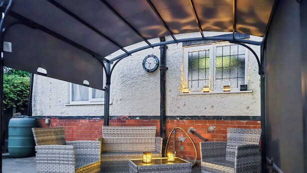 Ein überdachter Patio-Bereich mit Korbmöbeln und einer dekorativen Laterne.