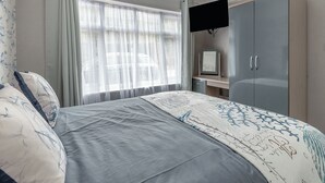 Ein Schlafzimmer mit Bett, Kleiderschrank, Schreibtisch und Fernseher.
