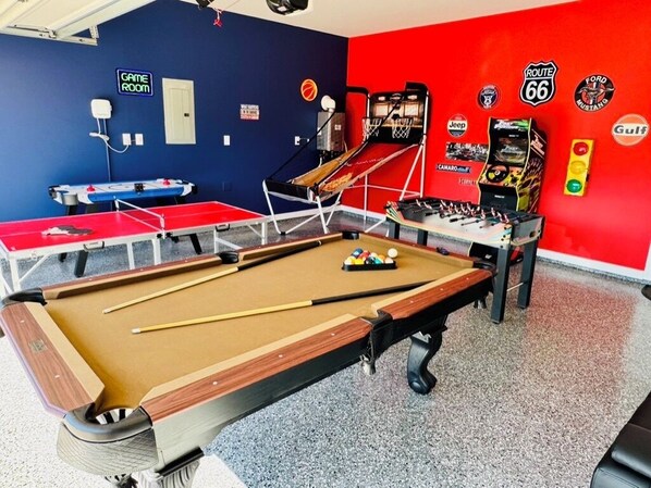 A pool table with a red and brown felt surface, a ping pong table, and a foosball table in a room with blue and red walls.