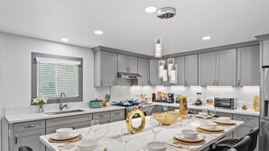 Una cocina moderna con una isla central, taburetes de bar y un comedor preparado para seis personas.