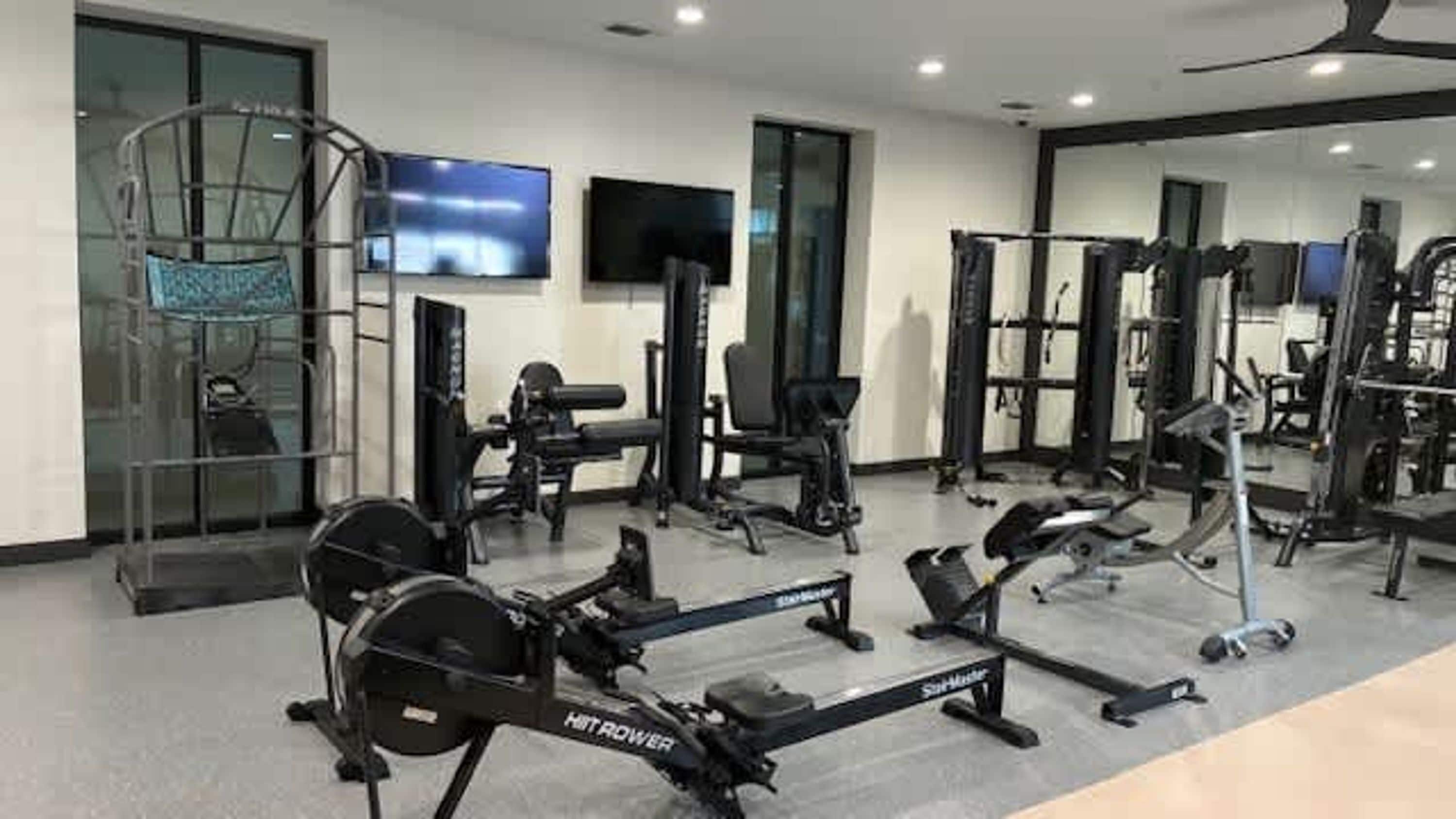 Ein Fitnessraum mit Ergometer, Krafttrainingsgeräten und einem Fernseher.