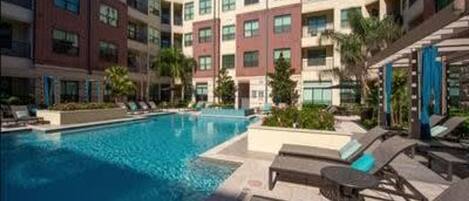 A hotel with a swimming pool, lounge chairs, and a multi-story building with balconies.