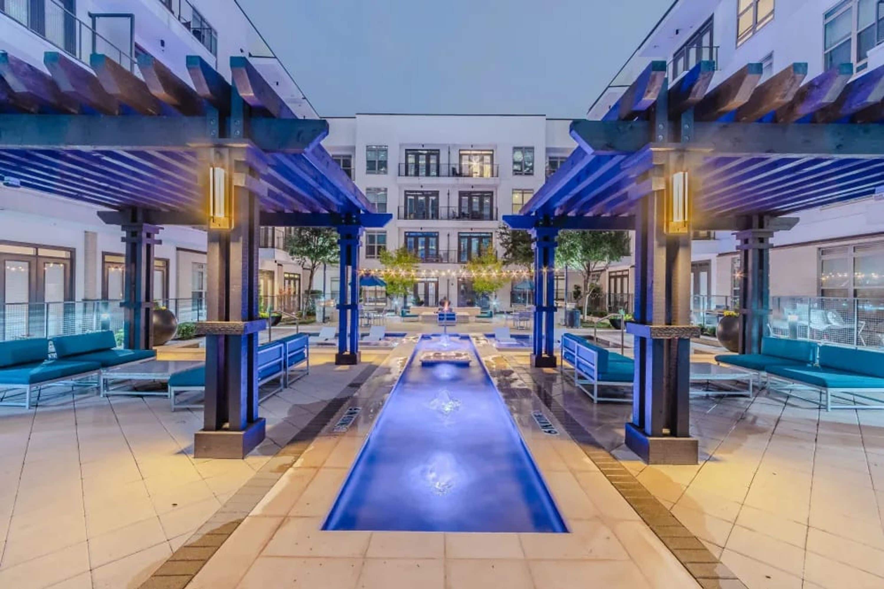 A modern outdoor pool area with blue seating and a central water feature.