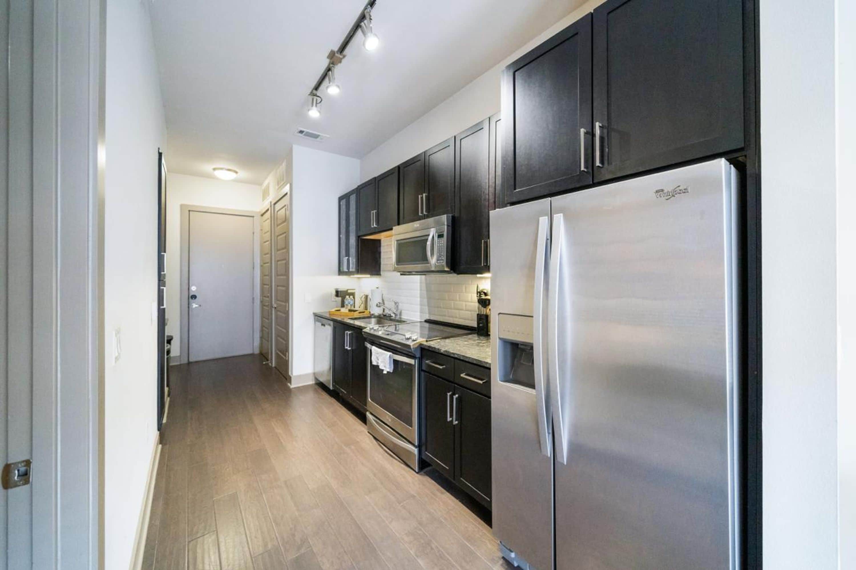 A modern kitchen with dark cabinetry, stainless steel appliances, and a wooden floor.