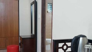 A small, clean room with a wooden wardrobe, a red stool, a small table with a kettle and a glass, and a mirror on the wall. - Sukh Sagar Resort (Kaliganj)